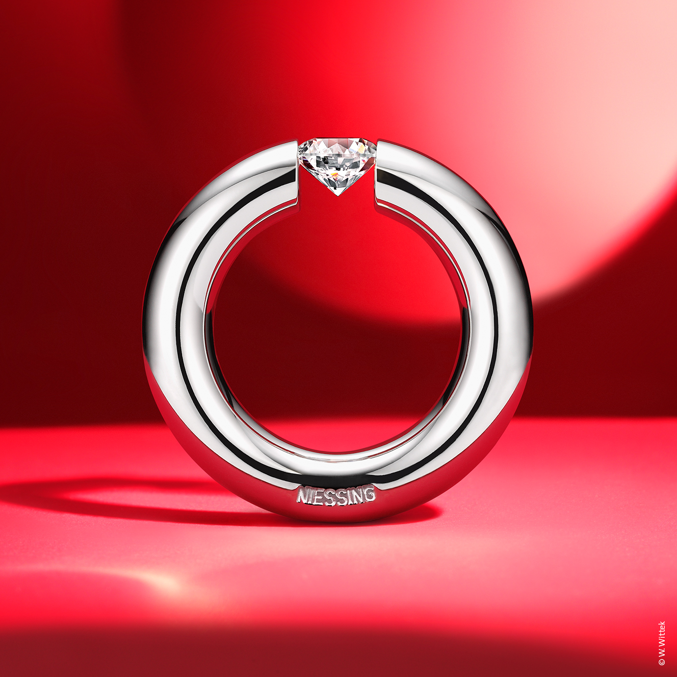 Runder Ring mit eingefasstem Stein auf rotem Hintergrund