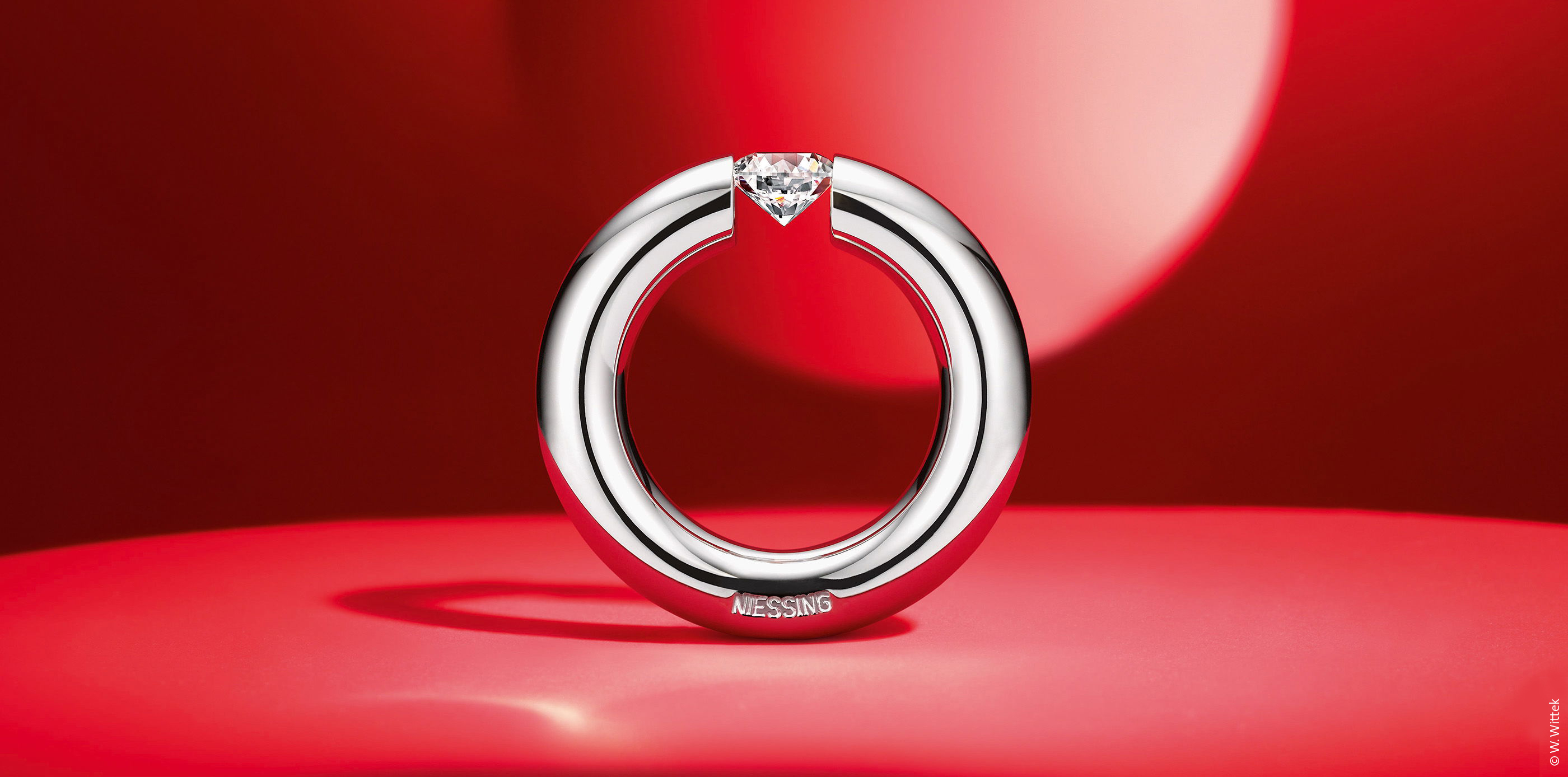 Runder Ring mit eingefasstem Stein auf rotem Hintergrund